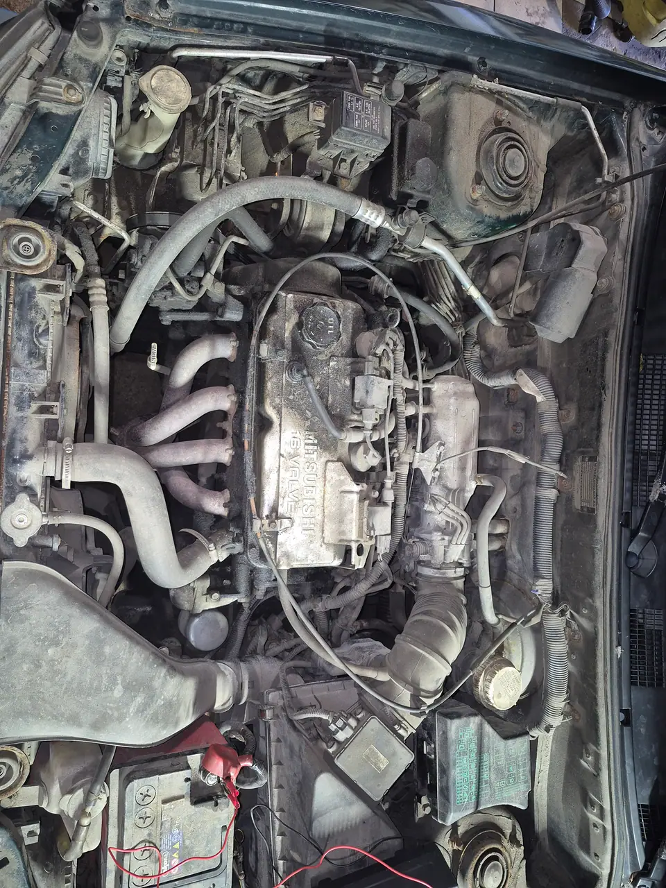 До: Моторный отсек Mitsubishi сверху до чистки: двигатель 16 VALVE, шланги и кузовные чашки покрыты пылью